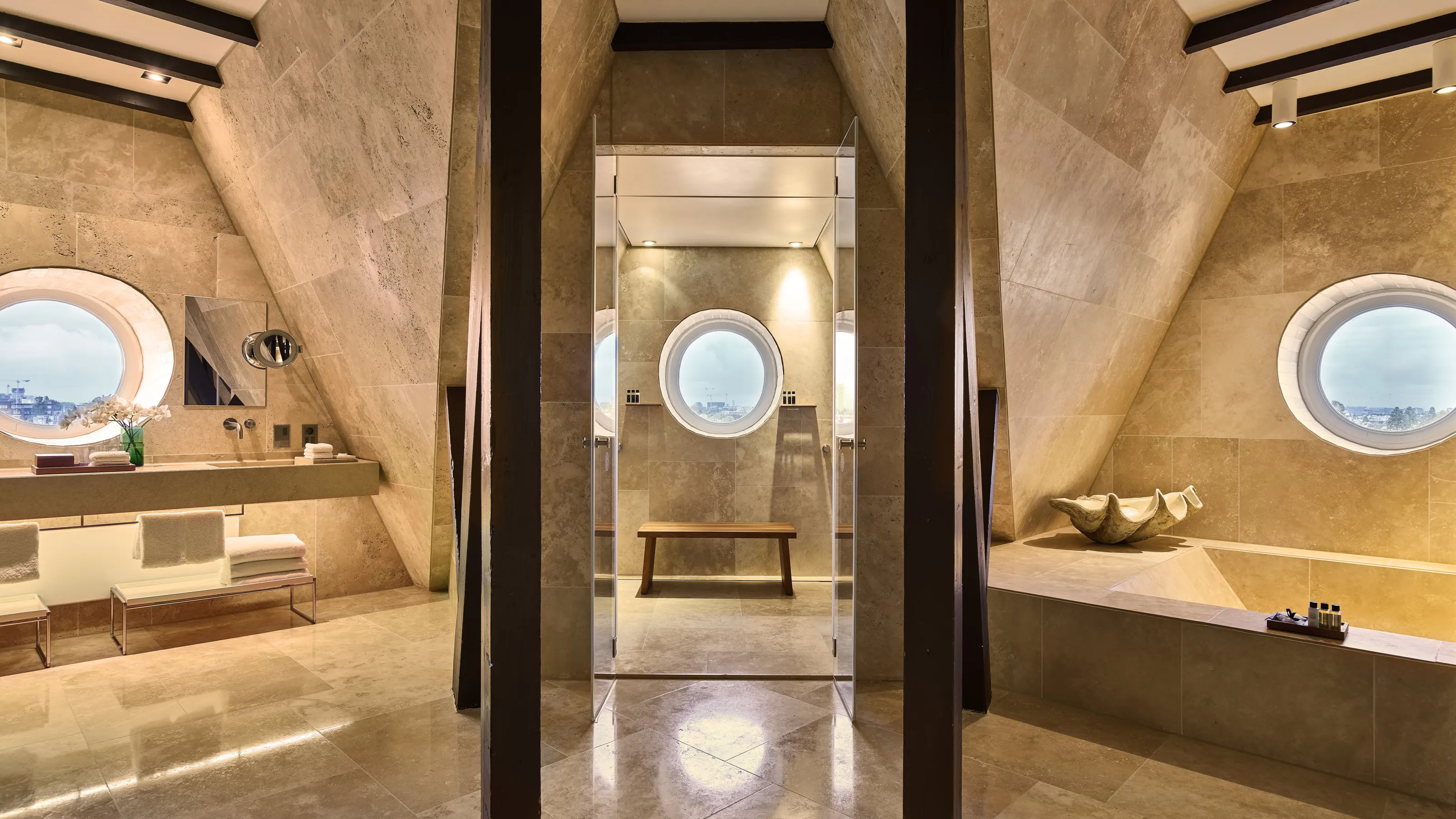 Minimalist spa bathroom with travertine walls, arched mirror niche, and skylights