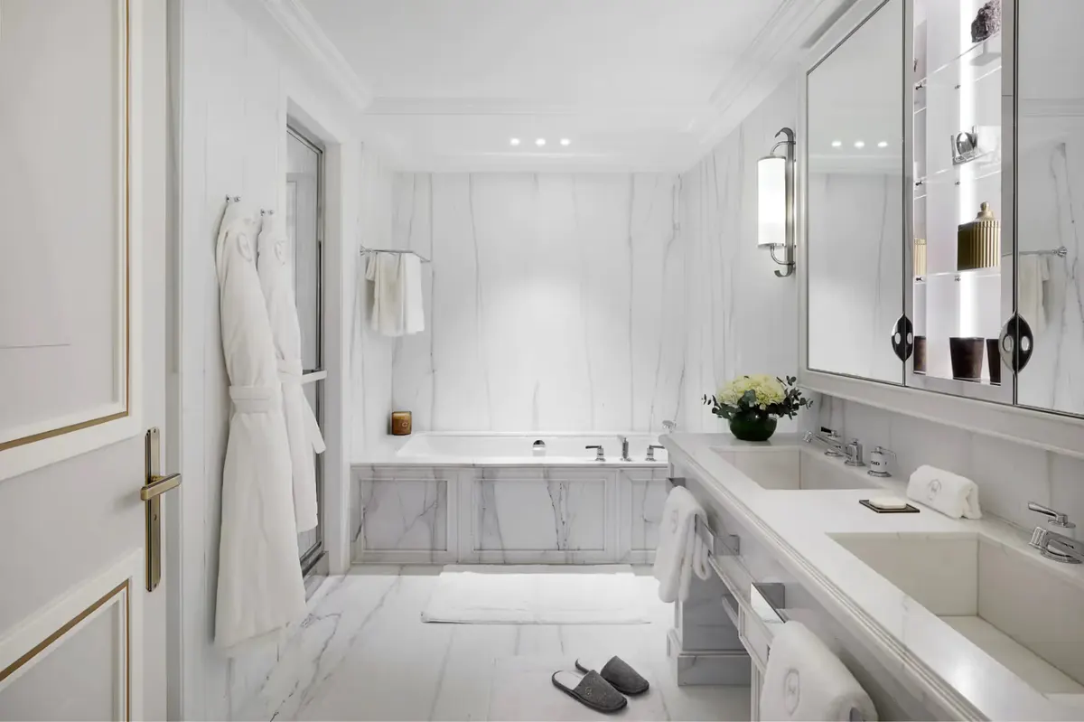 A bathroom with white marble walls, soaking tub, vessel sink, and marble floor