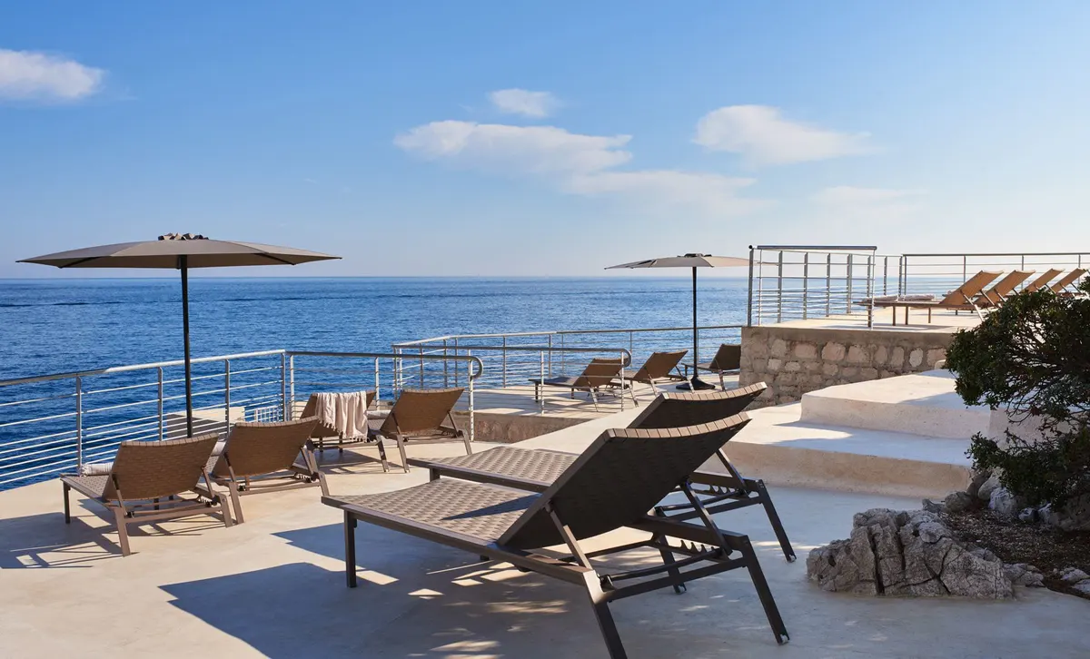 A poolside lounge area with sun loungers and umbrellas overlooking the Mediterranean Sea