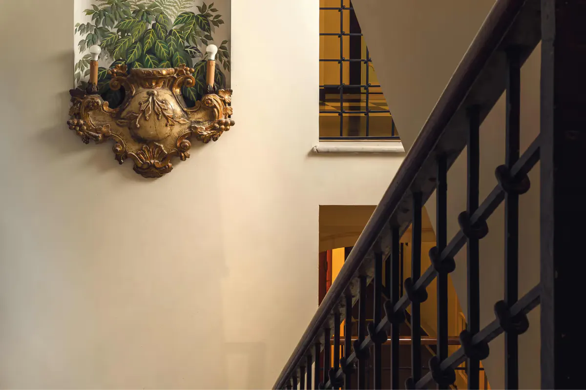 A staircase with iron railing beside climbing ivy on a pale stone wall