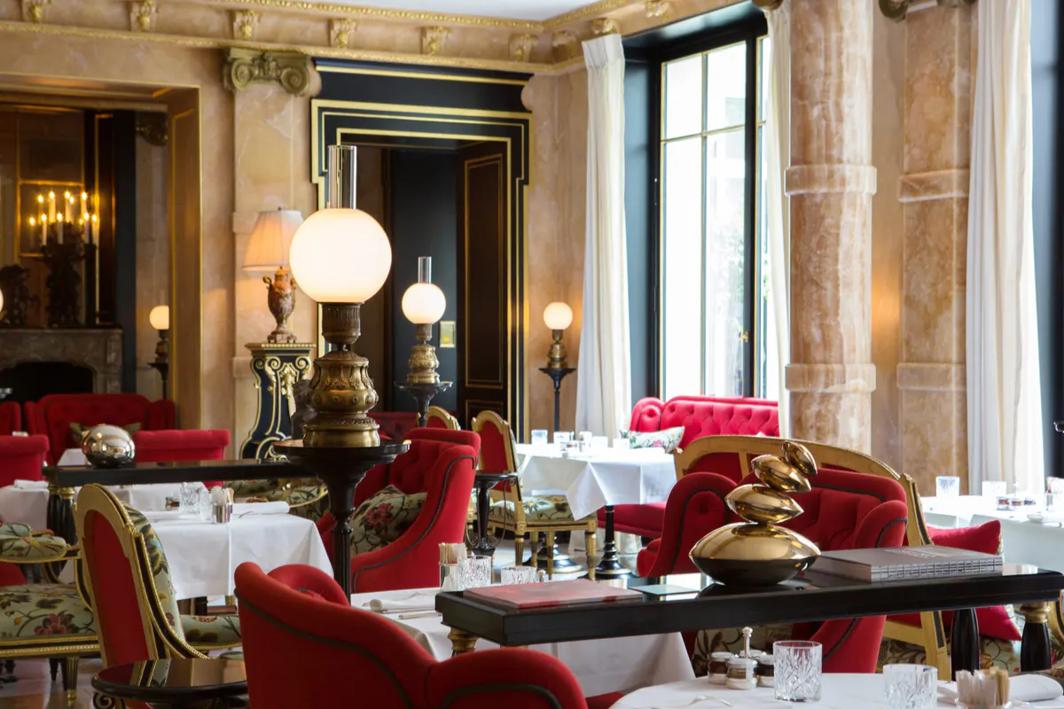A dining room with cream walls, soft pendant lighting, and red velvet banquettes