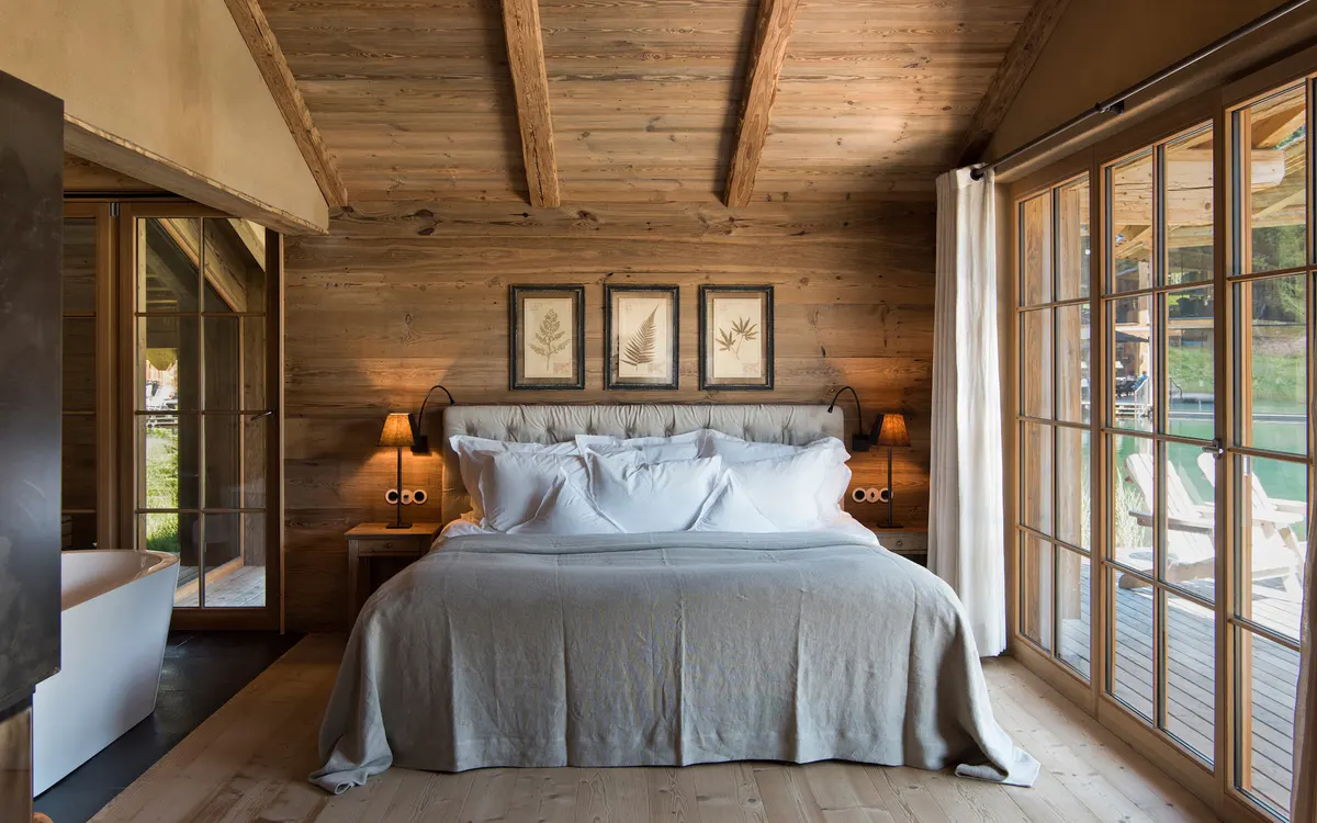Wooden bedroom with white bedding, wooden nightstands, and glass terrace doors