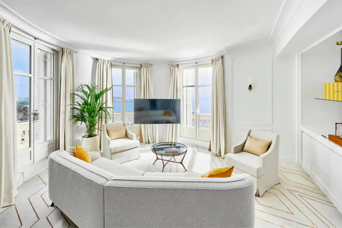 Suite living area with light gray sofa, multiple windows, and furnishings in cream and yellow tones