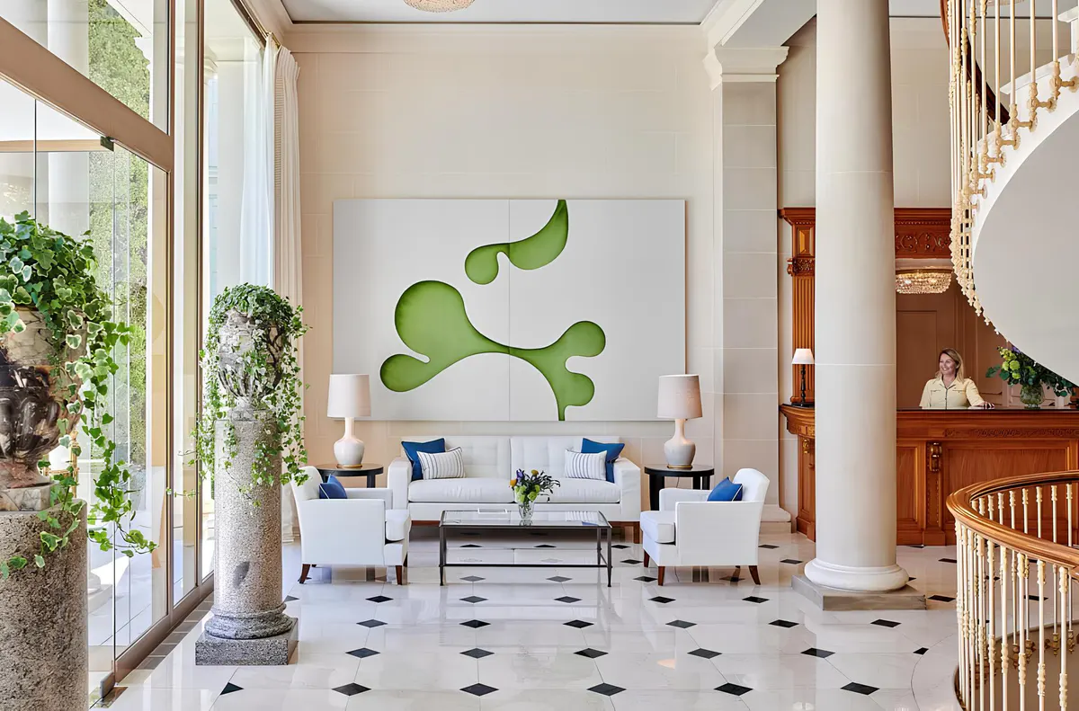 A high-ceilinged reception space with tall windows, arched artwork, seating areas, and terrazzo flooring
