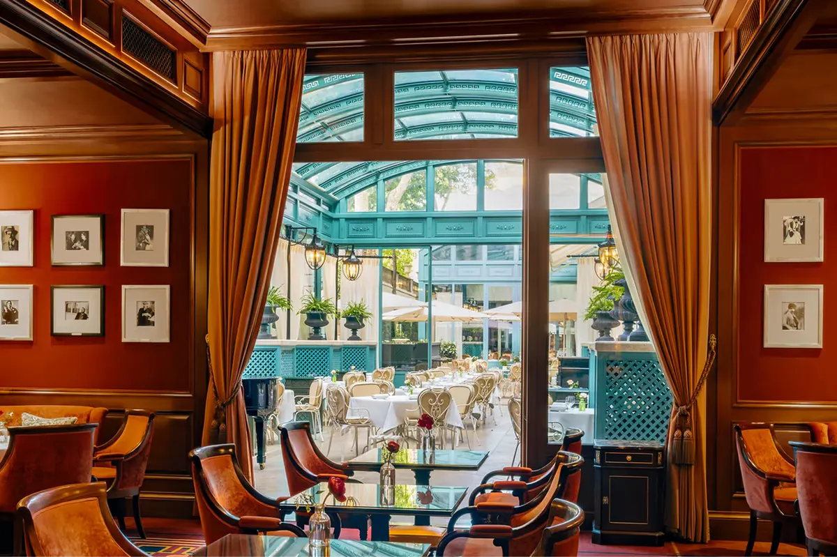 An intimate bar lounge with dark wood, green leather seating, and portrait artwork