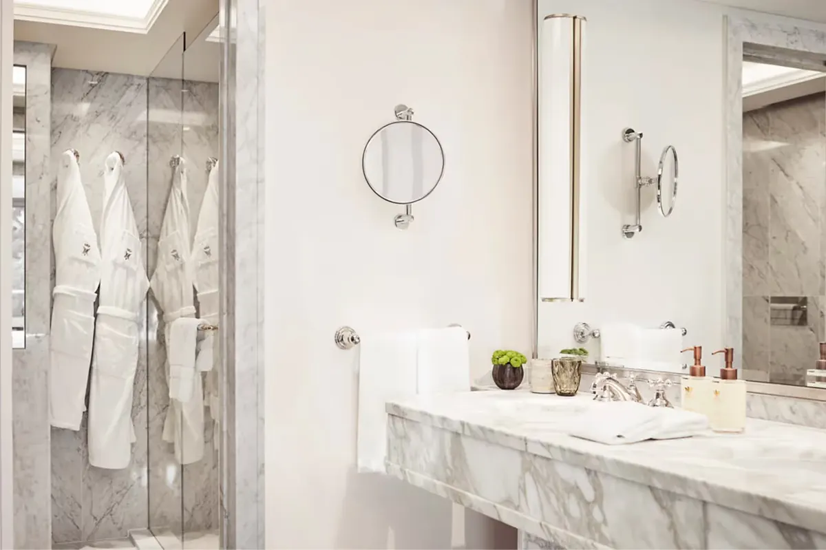 A marble bathroom with dual sinks, mirrored walls, and glass shower enclosure