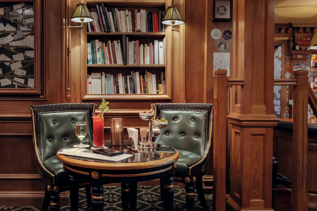 A library lounge with green leather chairs, wooden cabinetry, and intimate round table
