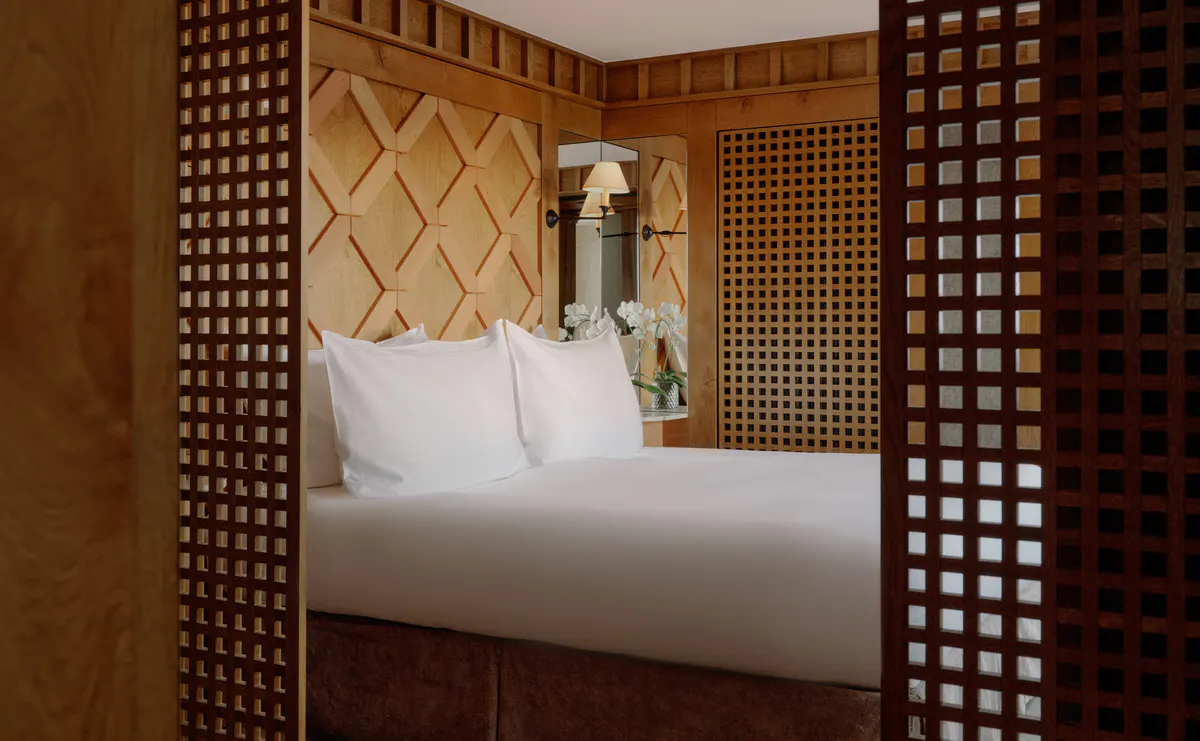 Bedroom framed by open wood lattice doors, with a diamond patterned headboard and white bedding