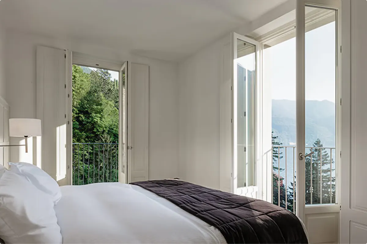 Bright bedroom with white linens and large windows overlooking the lake