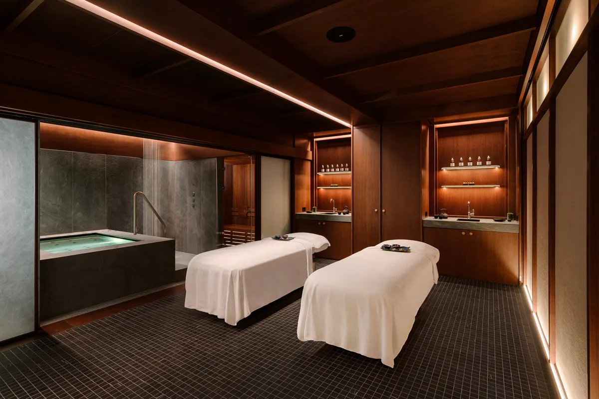 Spa treatment area with two massage beds, warm wood tones, and soft ambient lighting