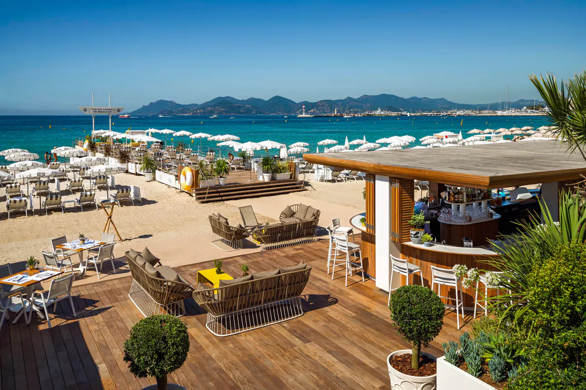 Beach club deck overlooking the Mediterranean with lounge beds and umbrellas in cream and blue tones