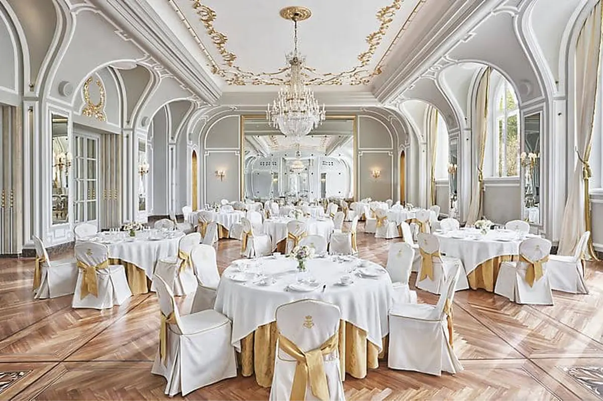 Formal banquet hall with gold chairs, white linens, and arched architectural details