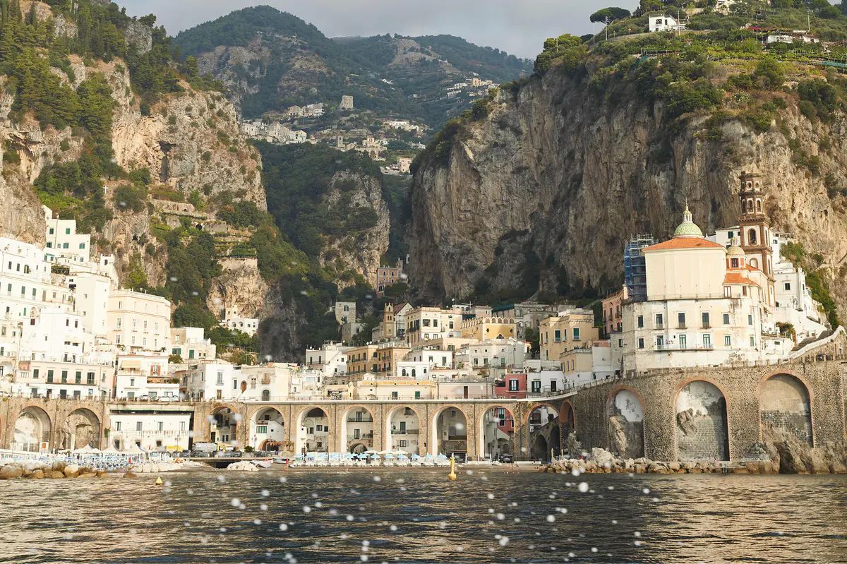 Waterfront village set in cliffs with colorful buildings, harbor boats, and mountain backdrop