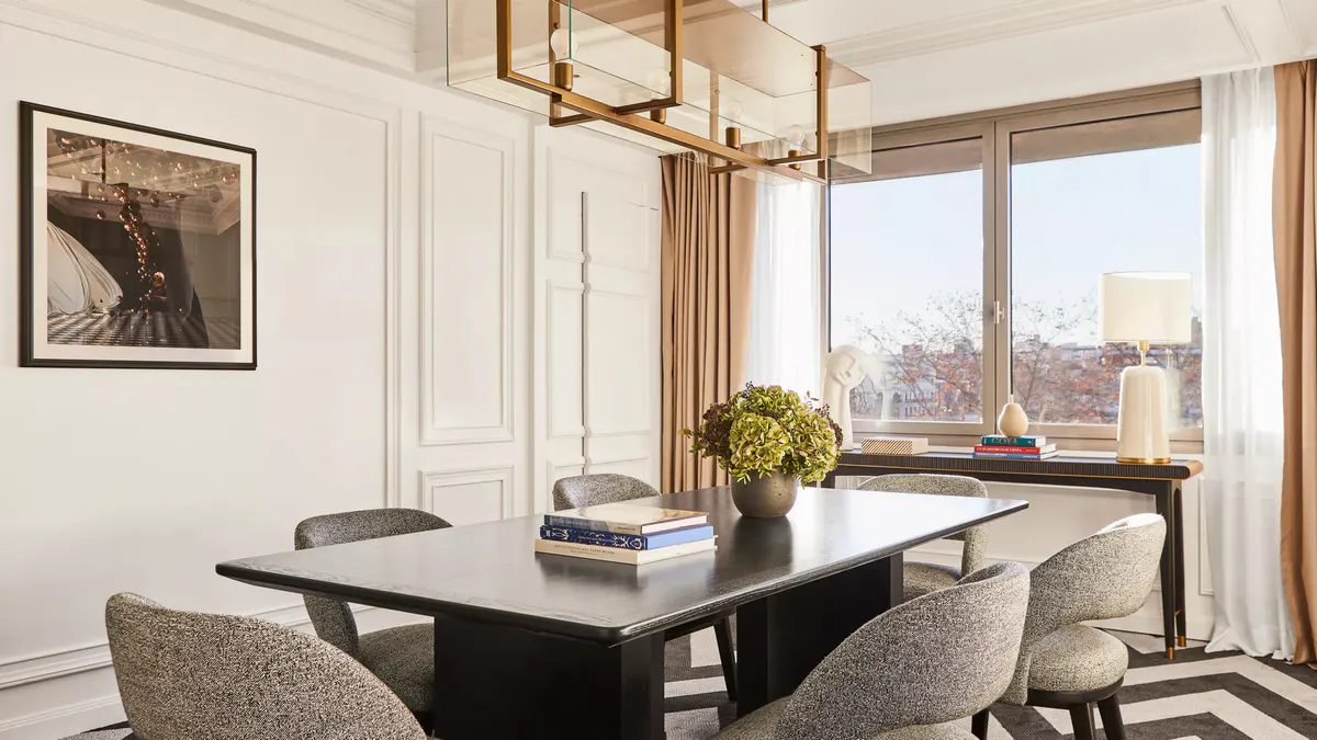 A suite with a black desk, city skyline windows, and neutral upholstery in warm tones