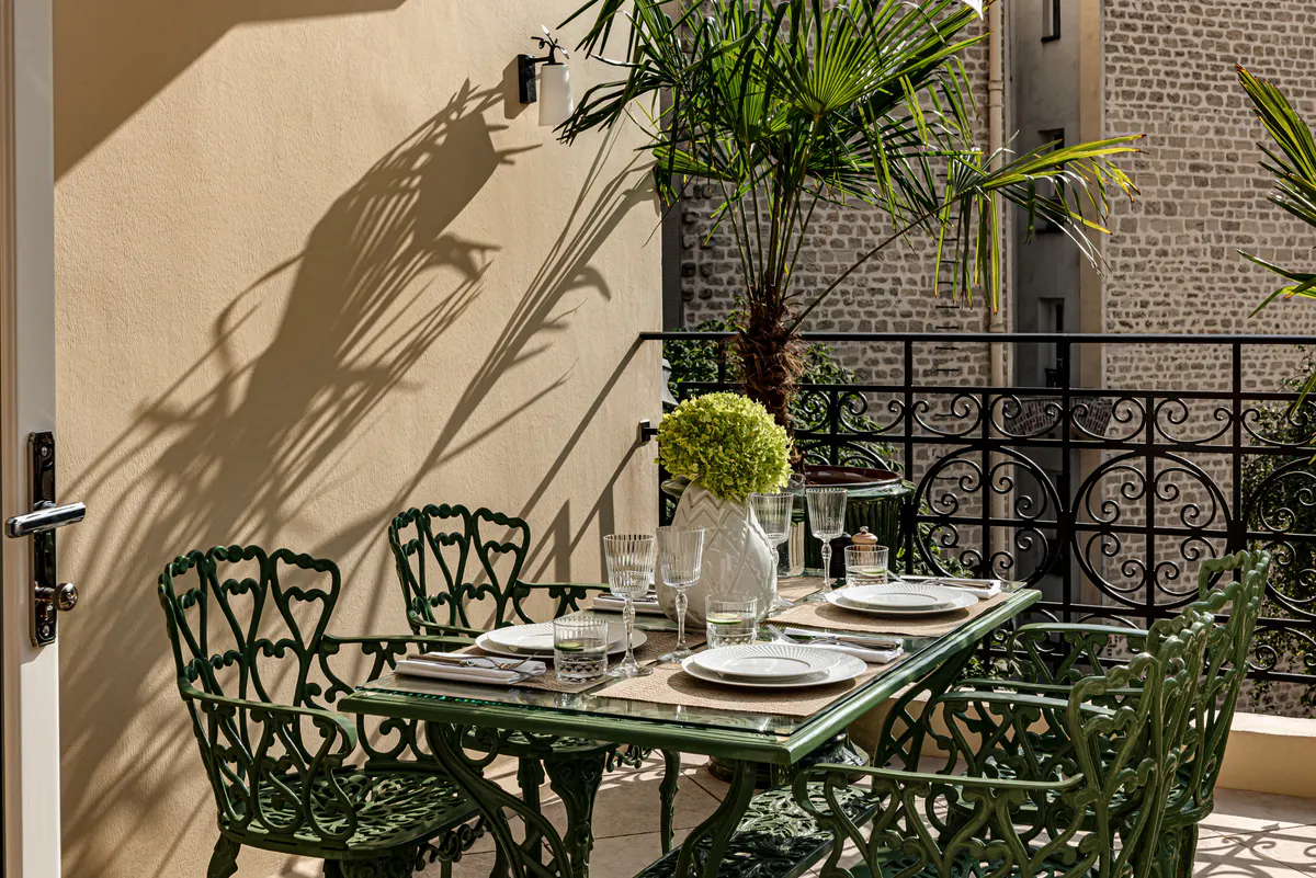 Wrought-iron bistro chairs on shaded garden patio, afternoon light casting shadows on stone