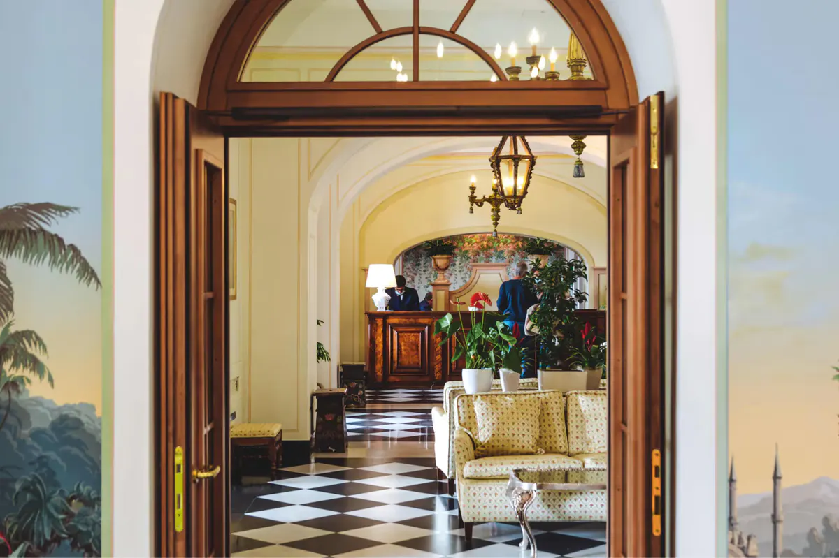 An arched entryway with dark wooden doors opening into a corridor with checkered floor