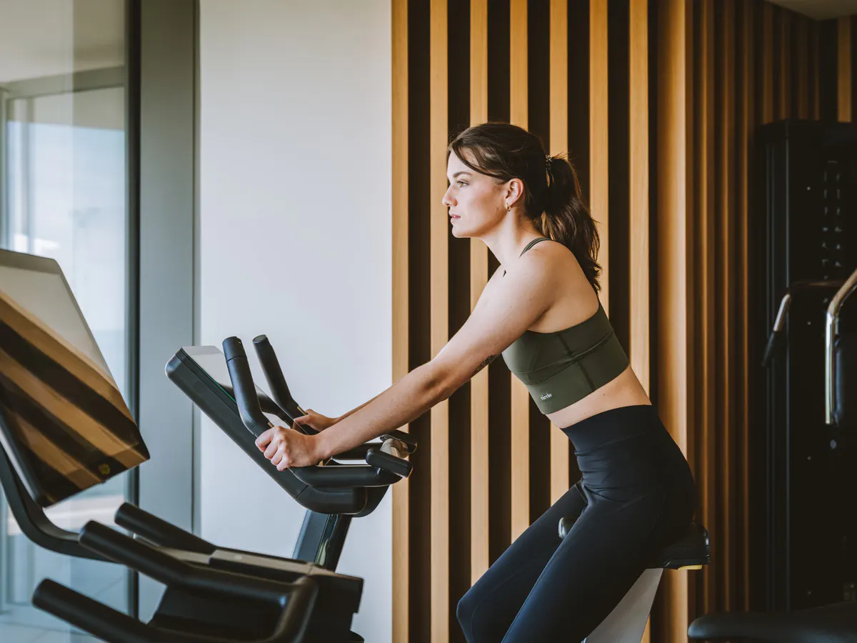 Woman on exercise bike in fitness room with striped accent wall and natural lighting