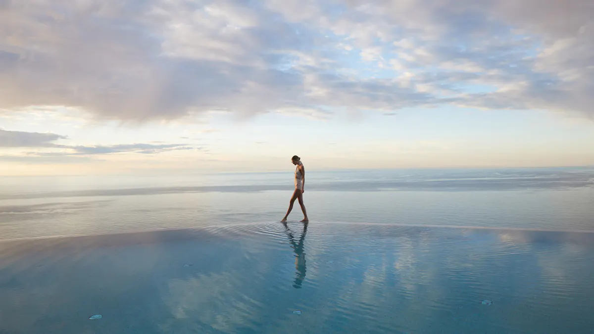 Figure at infinity pool mirroring sky and water