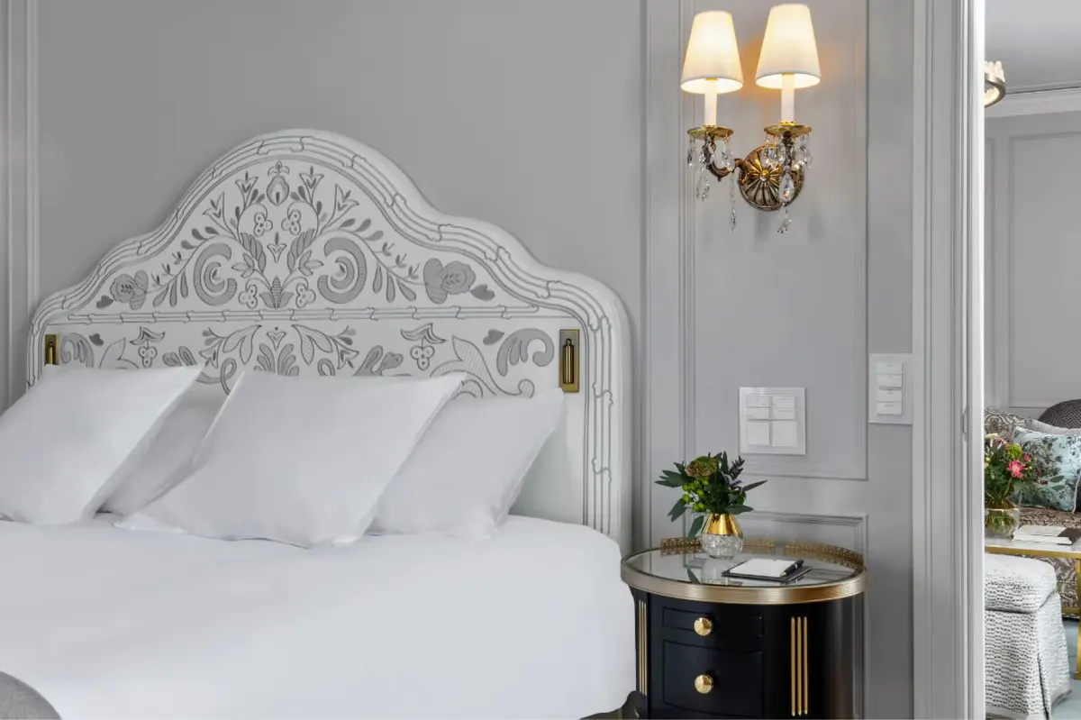 Bedroom with ornate white headboard, gold sconces, and bedside nightstands