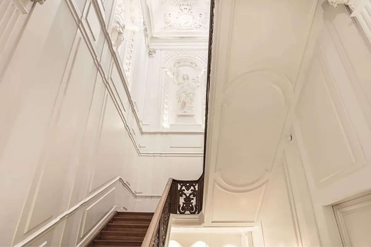 A stairwell with white paneled walls, arched skylight, and elegant railings creating a bright ascent