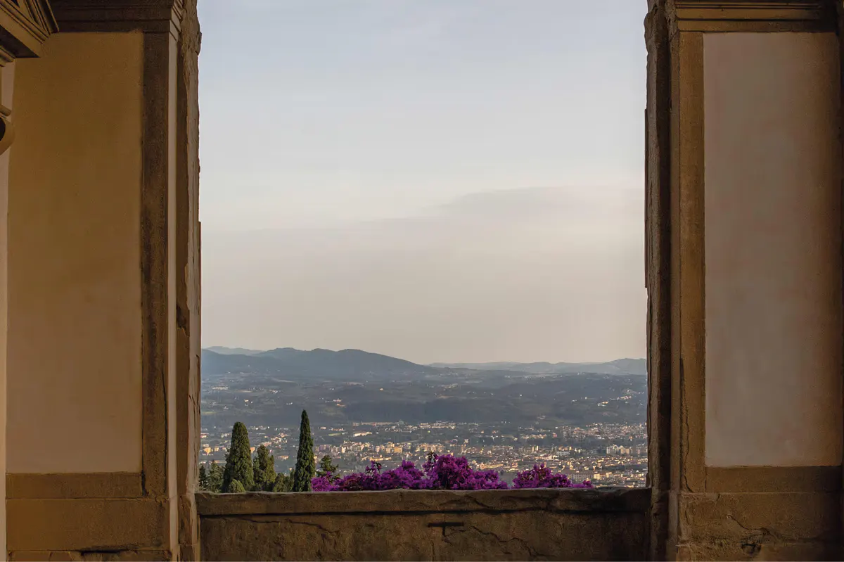 Stone window opening with magenta flowers, cypress trees, and sweeping view across the Tuscan countryside