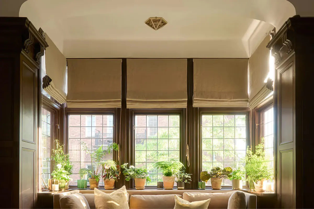 A window seat with large arched windows, cushions, and potted plants overlooking the exterior