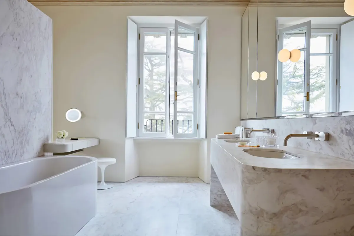 A marble bathroom with tub, freestanding sink, and French doors opening to terrace
