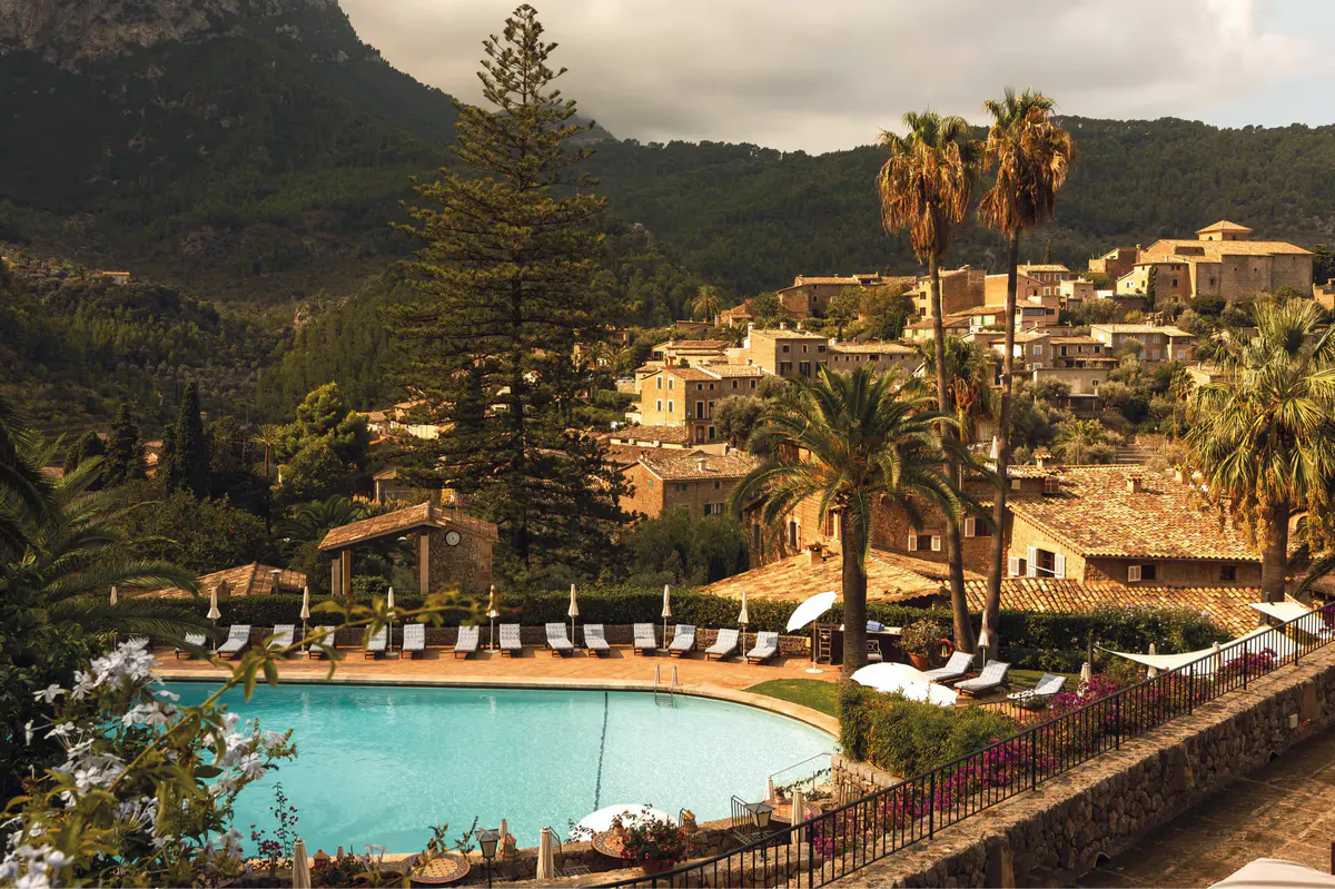Resort pool and buildings set in hillside with lounge chairs and Mediterranean backdrop