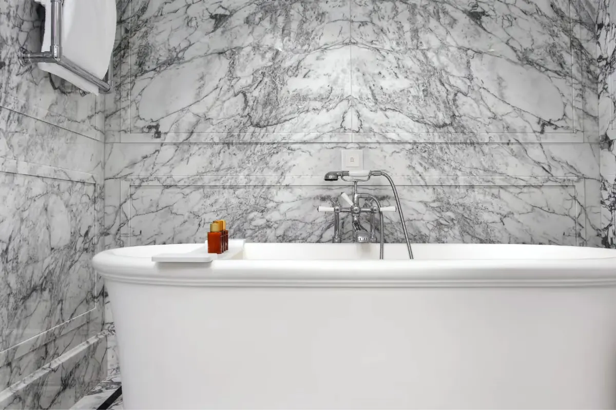 Marble bathtub surrounded by white marble walls with brass fixtures