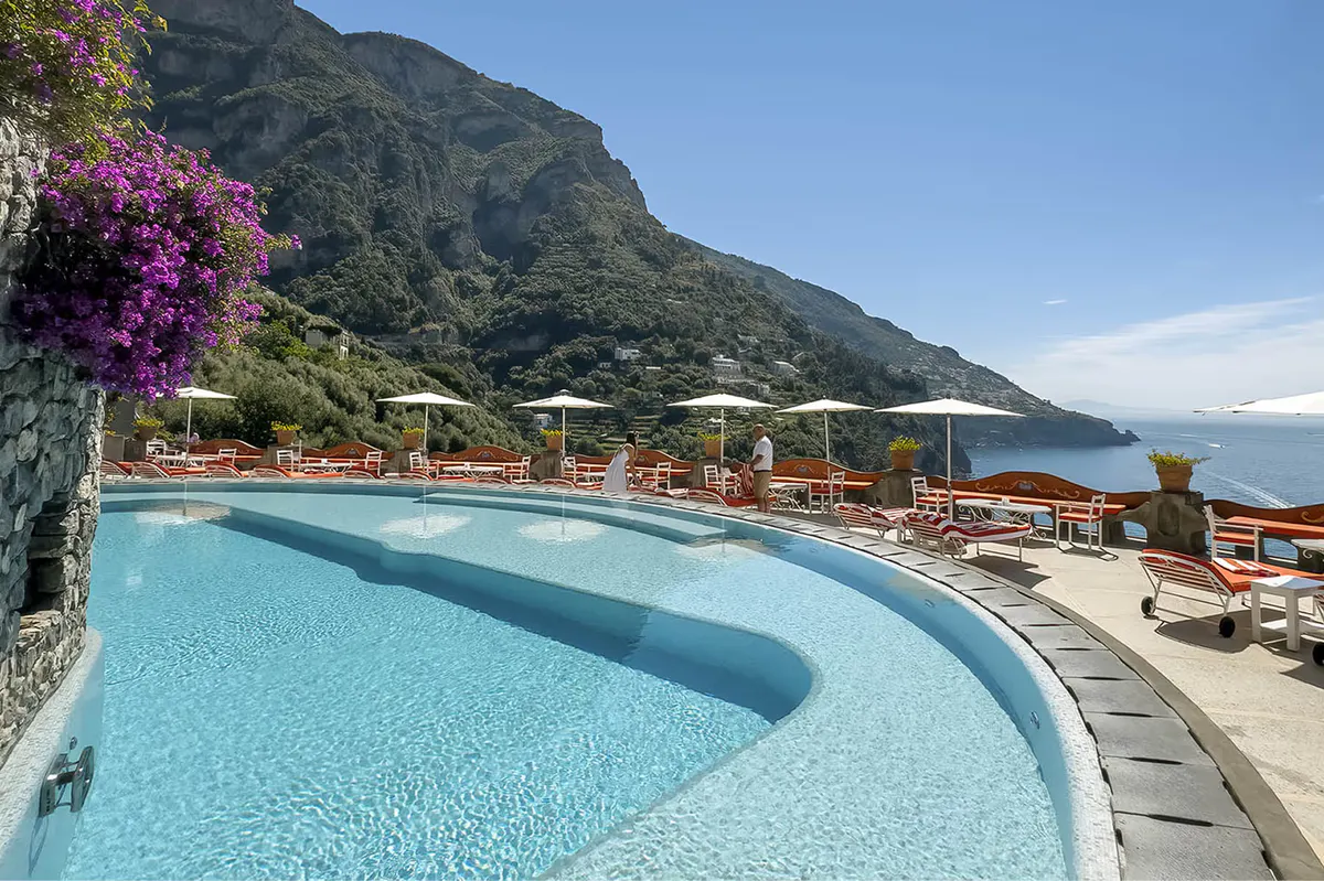 Curved infinity pool with turquoise water overlooking Mediterranean, flowering plants, and cliffside setting