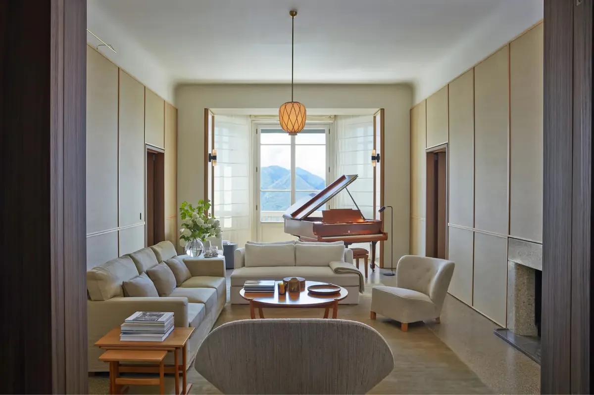 A salon with cream walls, tall windows, a wooden piano, and traditional furnishings