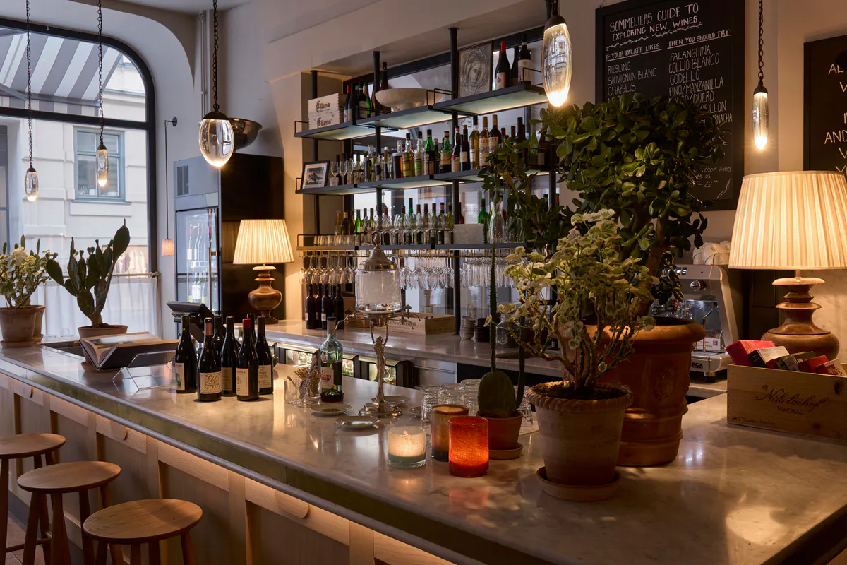 Bar area with shelves of bottles, lush greenery, and warm pendant lighting