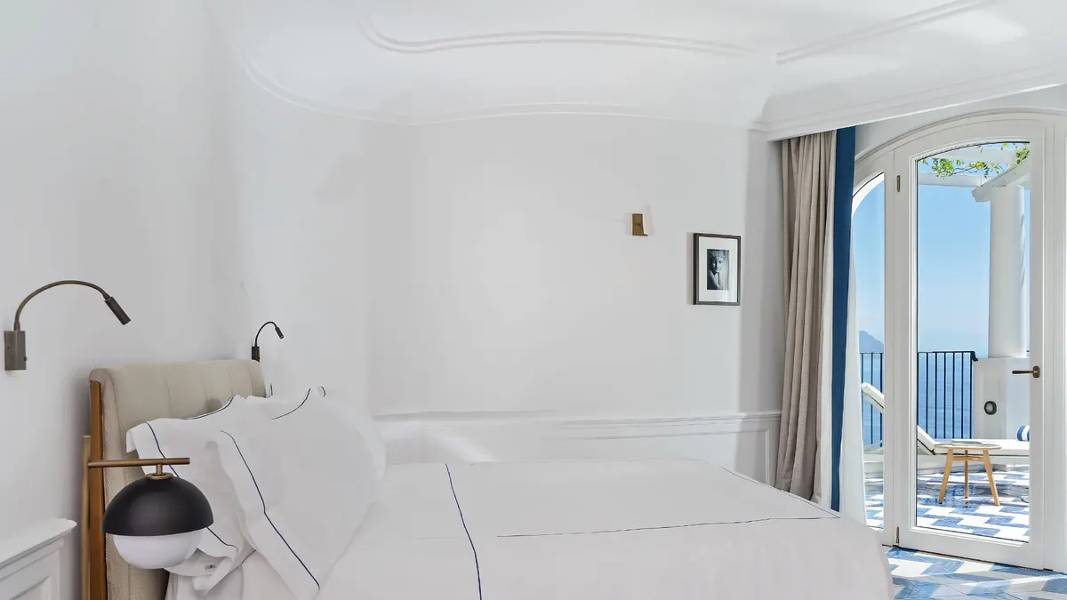 Minimalist bedroom with white bedding and ocean vista through glass doors at dusk