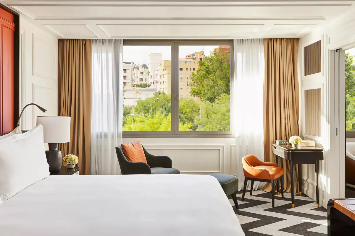A bedroom with window seating, warm gold curtains, and views of green rooftop gardens