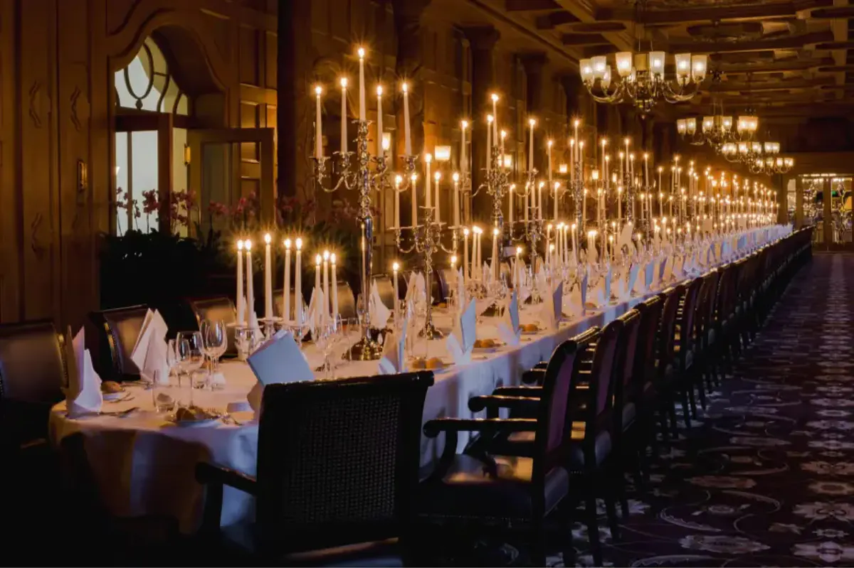 A long banquet hall with row of hanging pendant lights and formally set tables with white linens