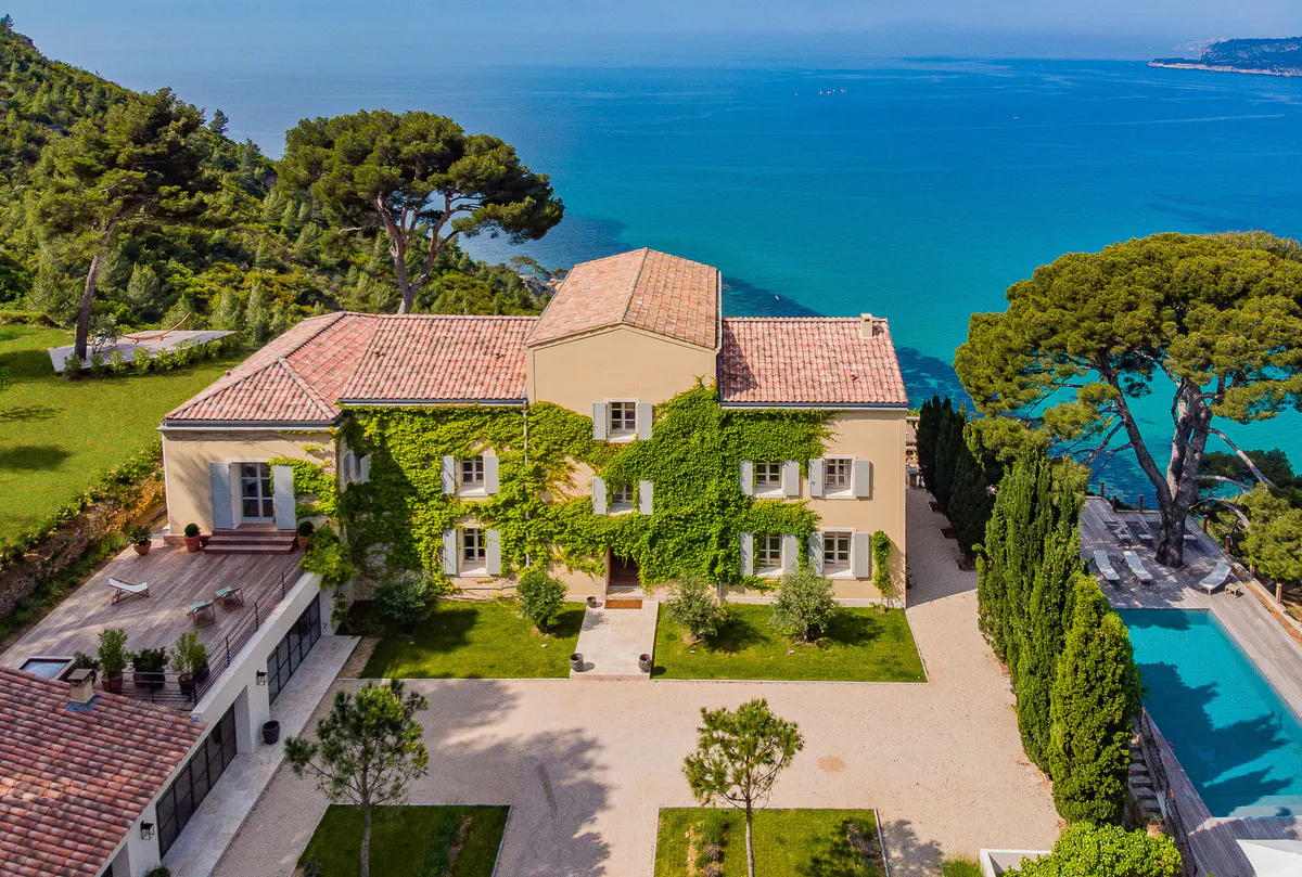 Ochre manor with clay tile roof set in green hillside, Mediterranean Sea beyond
