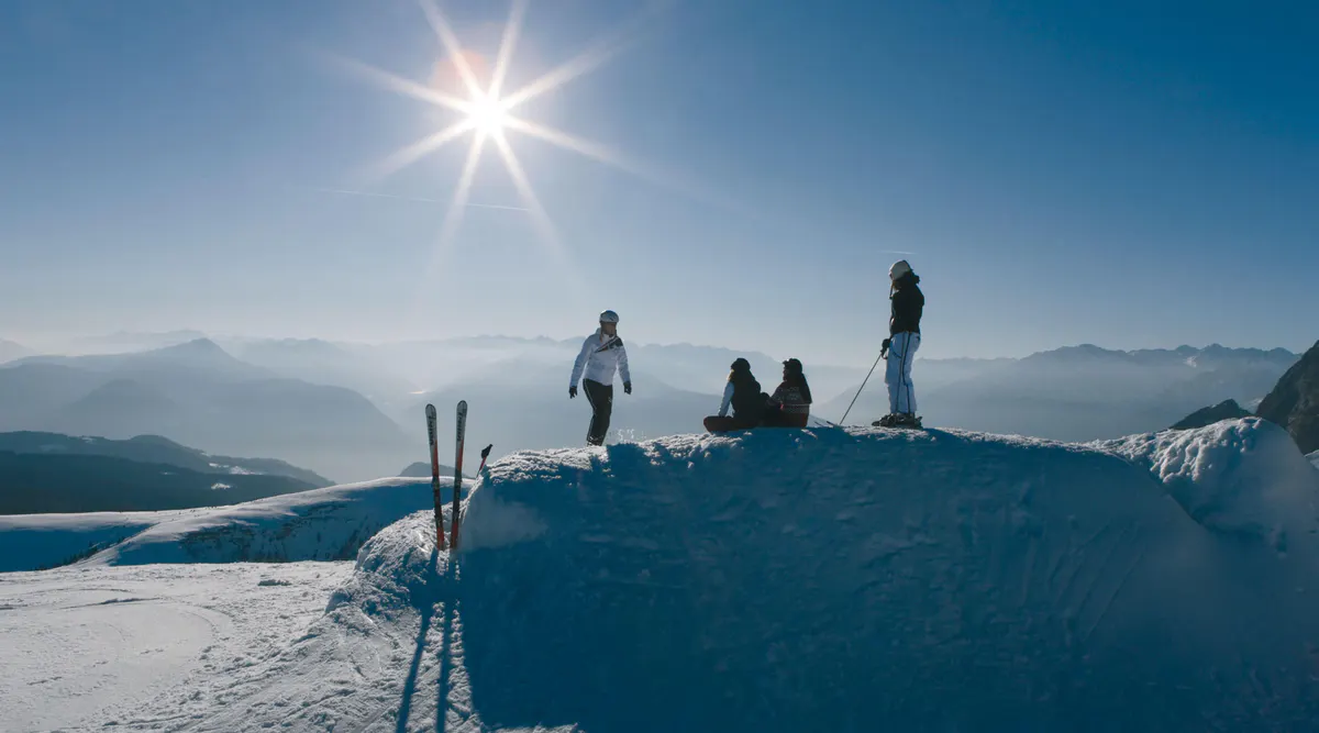 Group standing on snowy hilltop in clear sunlight with mountains visible