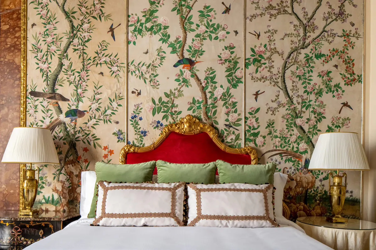 Bedroom with pale headboard upholstered in green, botanical mural behind bed, and brass bedside lights