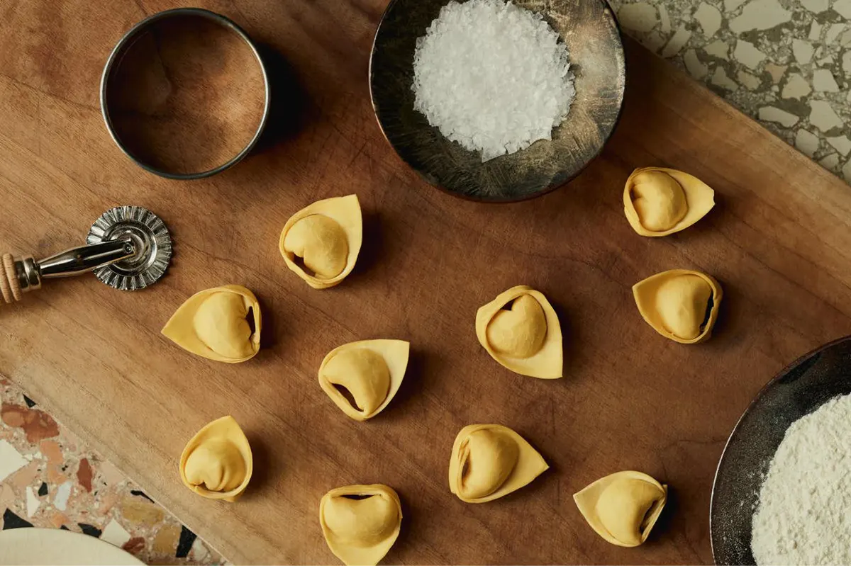 Handmade pasta arranged on a wooden board with flour and salt, artisanal food preparation