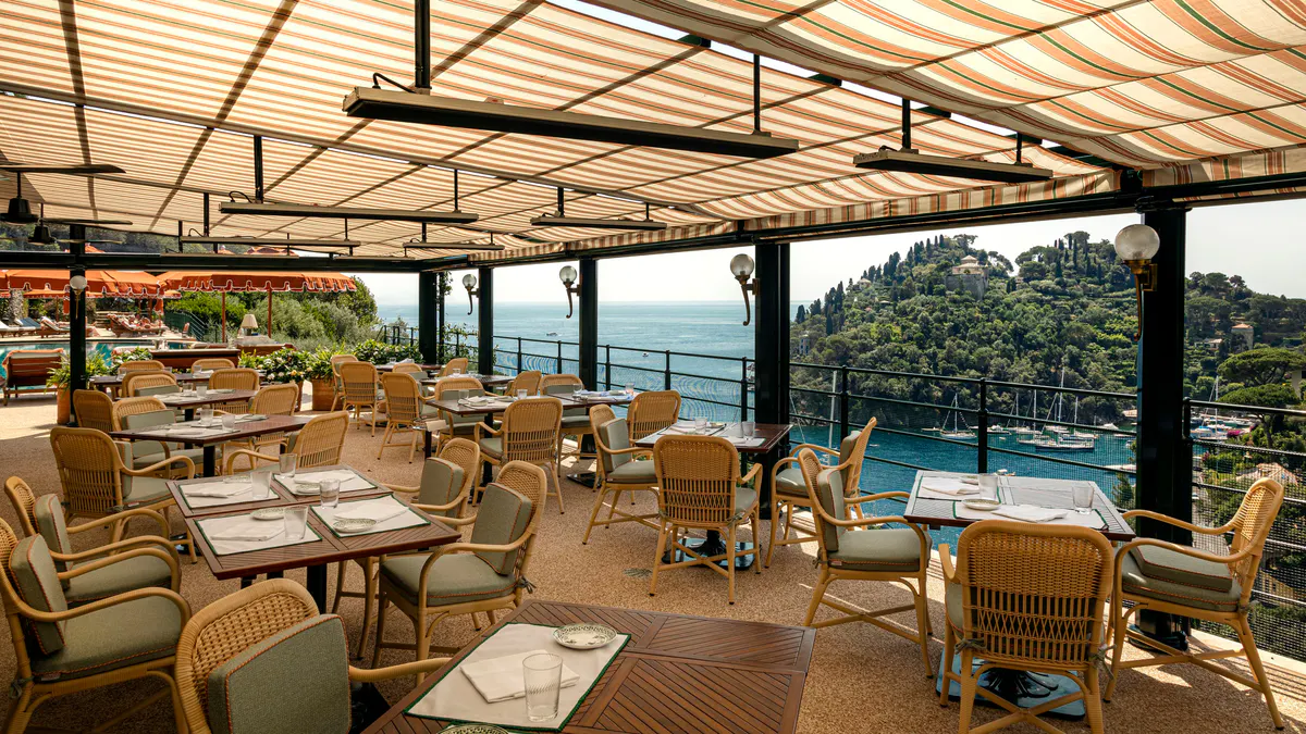 A sheltered dining pavilion with wood furnishings and turquoise harbor below