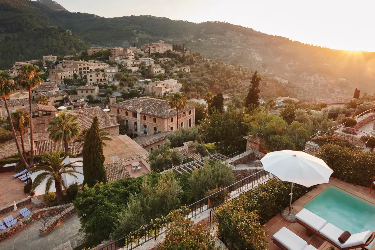 Resort buildings at sunset overlooking hillside with pool, cypress trees, and Mediterranean view
