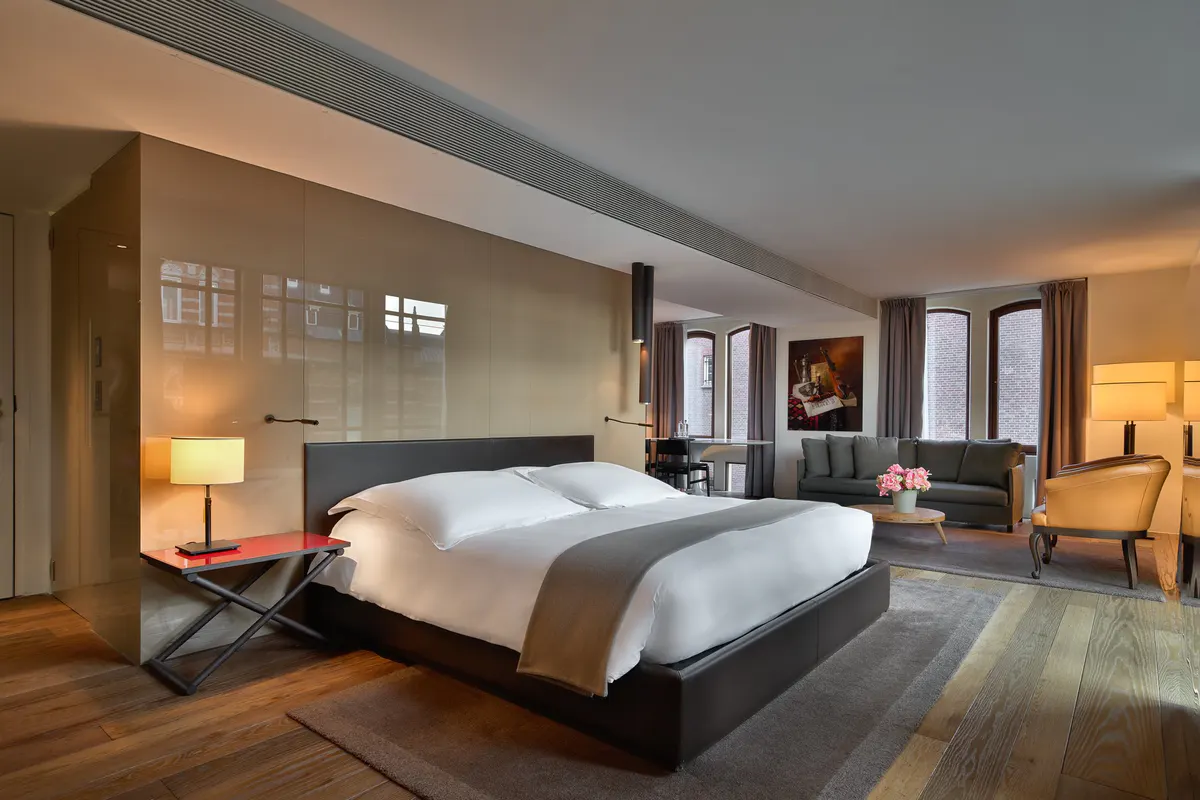 Spacious suite with dark wood bed frame, cream linens, window seating area, and warm lighting