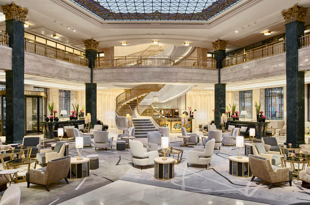 Grand lobby with columns, coffered ceiling, neutral seating arrangements, and skylight above