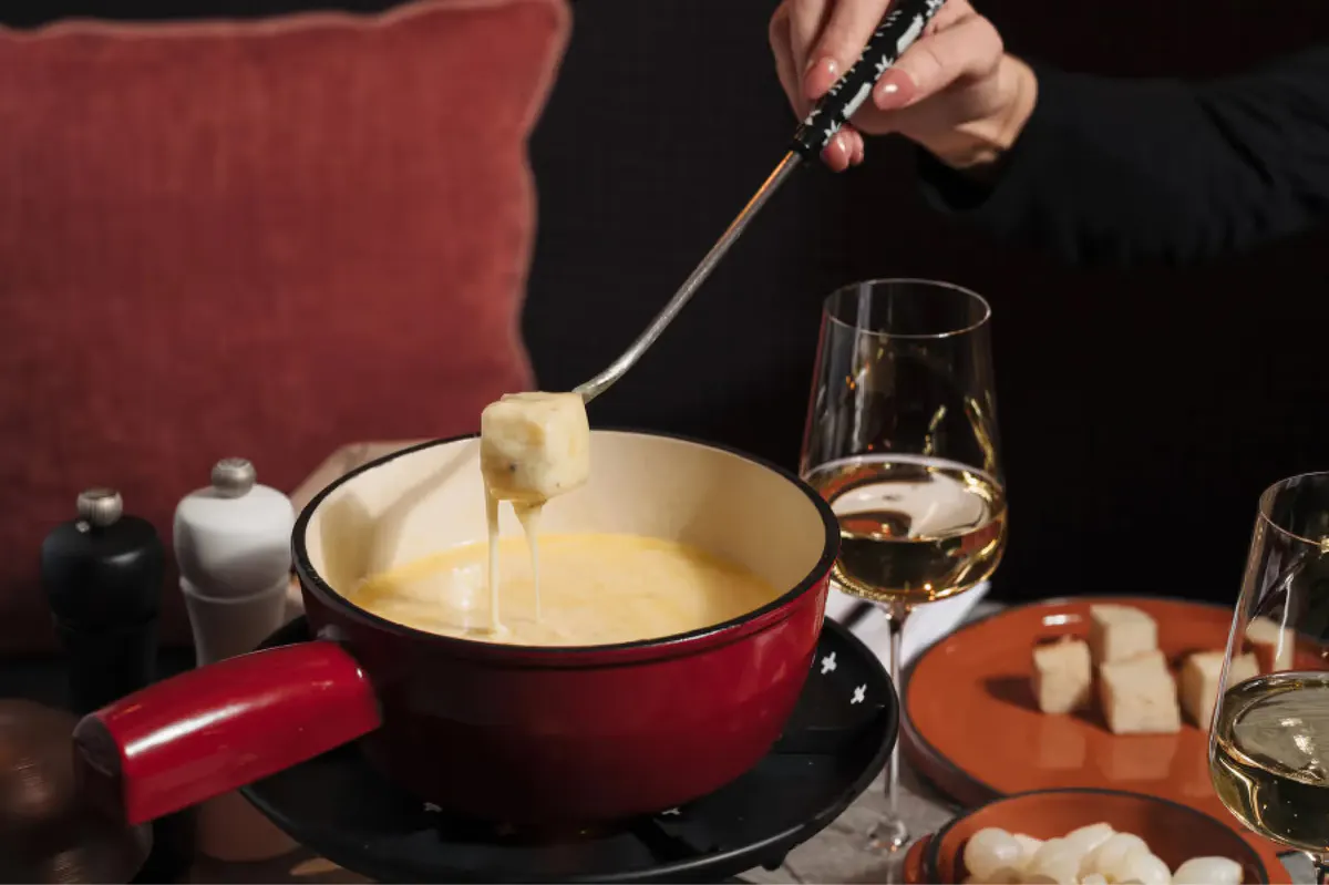 Fondue pot with melted cheese being stirred with fork over table service items