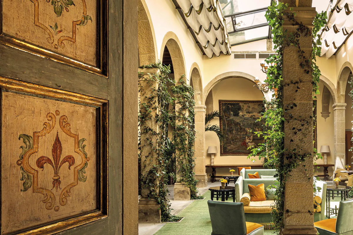 Vaulted courtyard with decorated wooden doors, climbing ivy, arched columns, and green seating with gold accents
