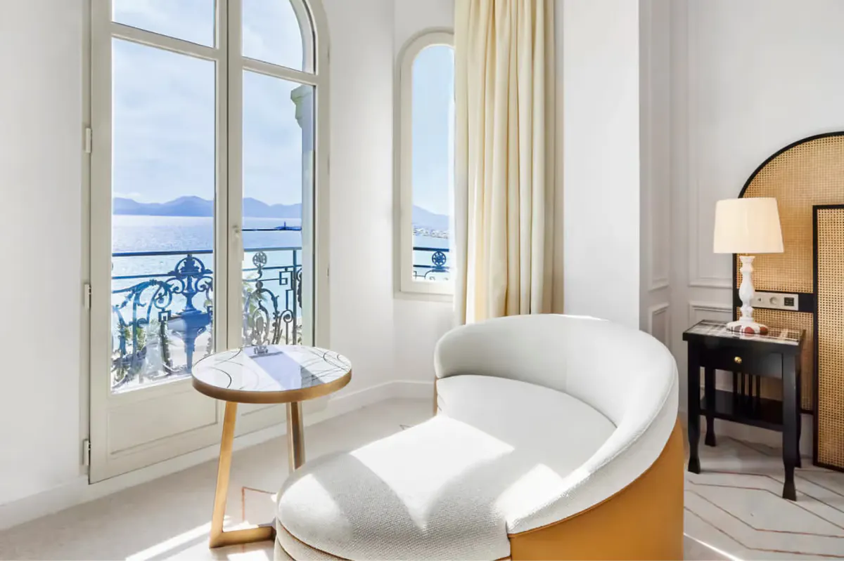 Curved white lounge chair by glass doors overlooking the Mediterranean, with sea views and a small side table