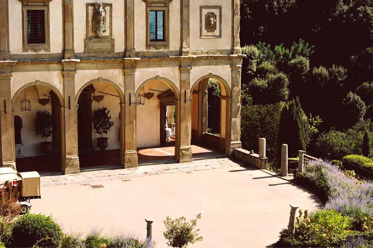 Vaulted courtyard with arched openings, dark wooden doors, terracotta flooring, and cypress beyond