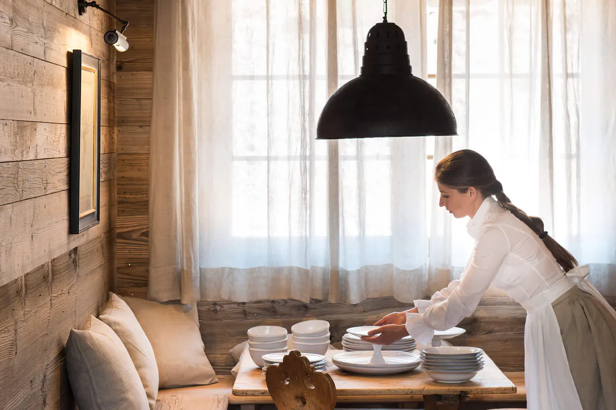 Staff member plating food in a bright dining room beneath black pendant light
