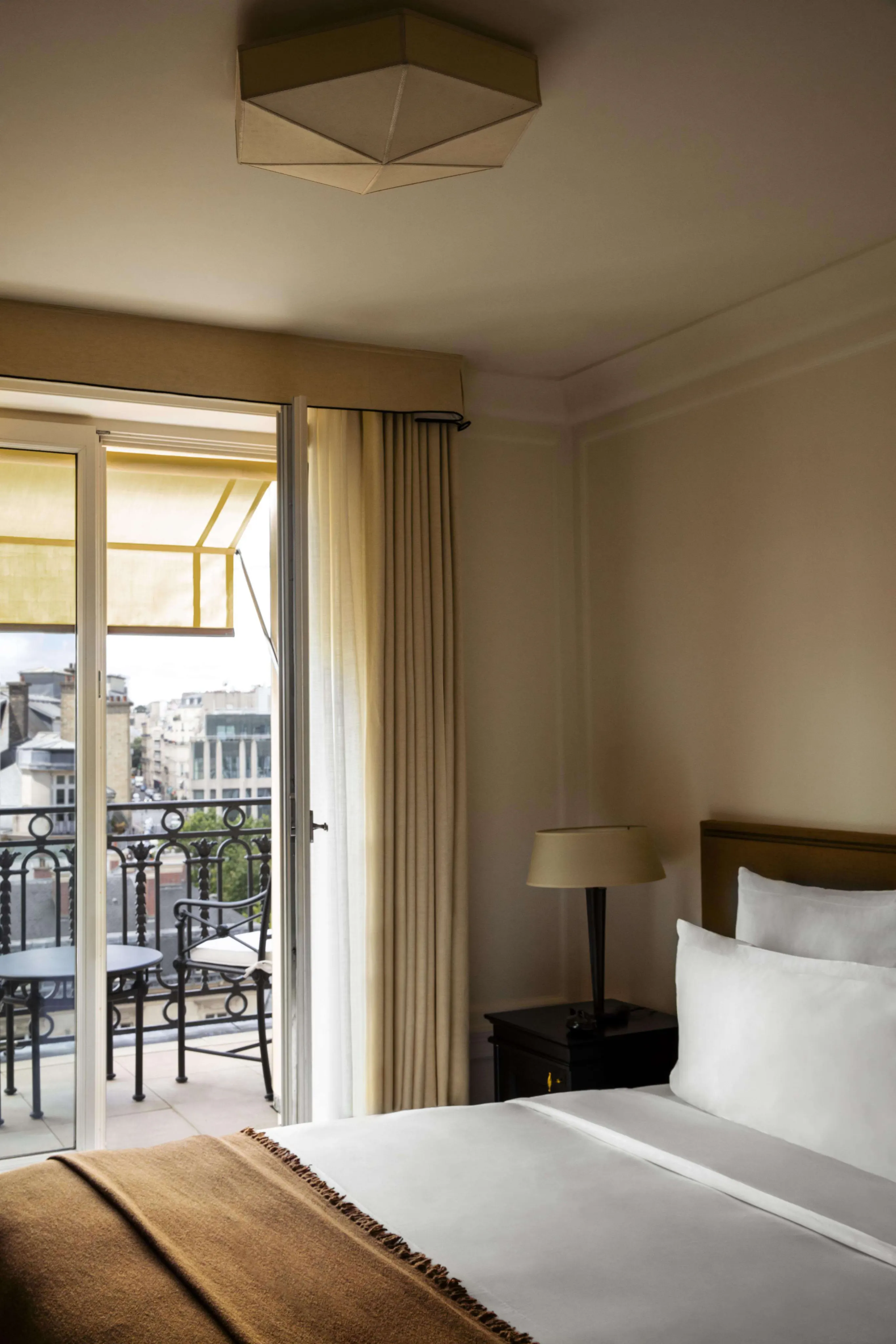A hotel bedroom with a balcony overlooking Paris rooftops and the city