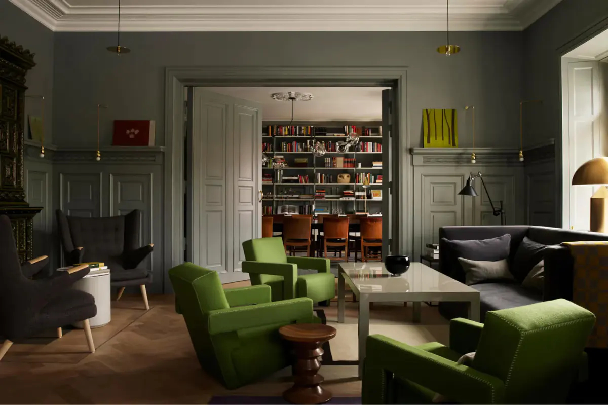 A library lounge with dark green armchairs, built-in bookshelves, art deco details, and reading lamps